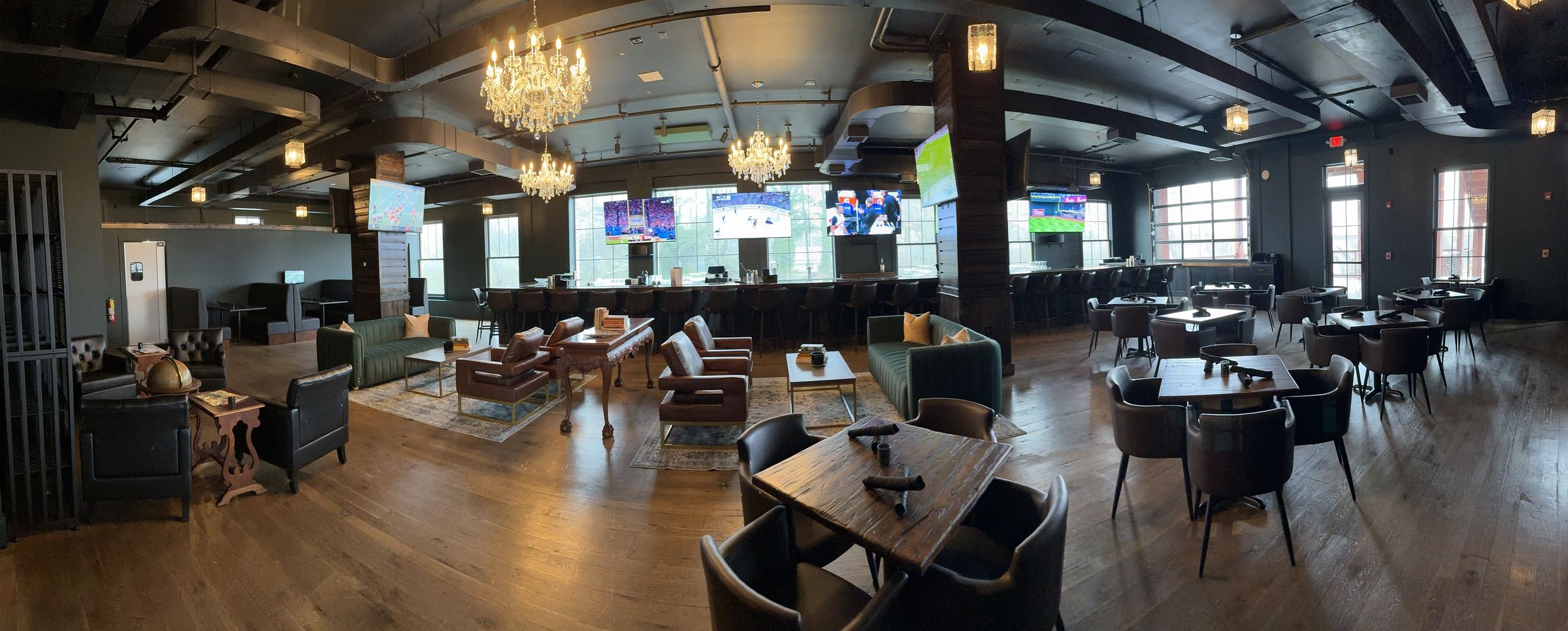 Wide view of the Suite 200 dining room in Milton, Georgia with chandeliers, emerald banquettes, leather club chairs and the long bar beyond